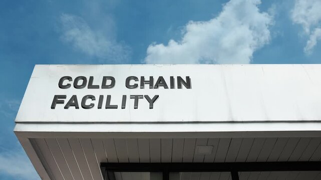 Cold Chain Facility word sign displayed on the large, industrial building facade beneath a clear blue sky, signifying a temperature-controlled logistics center for perishable goods storage 