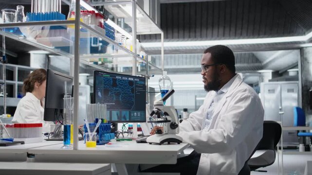 Clinical microbiologist using compound microscope for detailed sample observation using PC software. Biotechnology research facility worker studies tissue with optical device and computer, camera A
