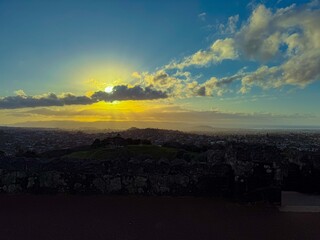Obraz premium The sun is setting into the horizon at the city. The view is from high ground green mountain in summer time. Beautiful orange sunset view of Auckland city.