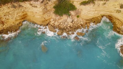 Aerial view of turquoise sea crashing into golden cliffs in Cephalonia, Greece
