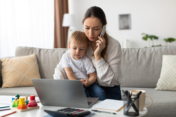 Mother speaks on the phone while her young child sits beside her, focused on a laptop. The cozy...