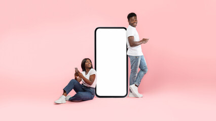 In a vibrant pink setting, a cheerful couple leans on a big smartphone screen. They are texting on their phones, enjoying each other’s company and modern communication.