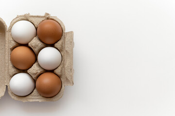 Top view of half dozen eggs arranged in alternating pattern of white and brown in open paper pulp egg carton, positioned on right side, isolated, white background, empty space on left, close-up
