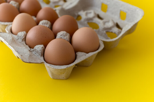 Open paper pulp egg carton with brown eggs, partially visible from side angle, isolated on yellow background. Close-up, concept of freshness and natural food. Shallow depth of field - Powered by Adobe