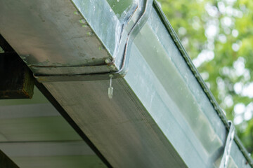 Leaking galvanized roof gutter joint with water dripping from worn-out seal