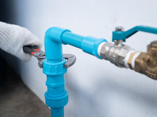 Plumber tightening PVC union fitting with pipe wrench on home water pump system