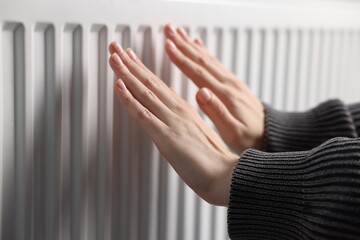 Woman warming her hands near radiator indoors, closeup