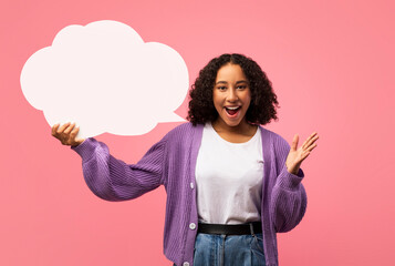 An enthusiastic young black woman is in a pink studio, joyfully holding an empty speech bubble while expressing her excitement. She smiles broadly, creating a lively atmosphere for creative designs.