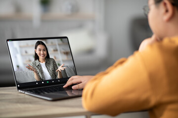 A cheerful young female teacher is conducting an online tutoring session with an unrecognizable overweight child at home. They are engaged in a video chat using a modern laptop.