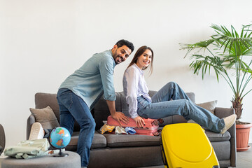 Fototapeta premium A couple joyfully sits on a couch, packing their luggage for a trip. They are surrounded by travel items and smiling, showing their excitement for the adventure ahead.