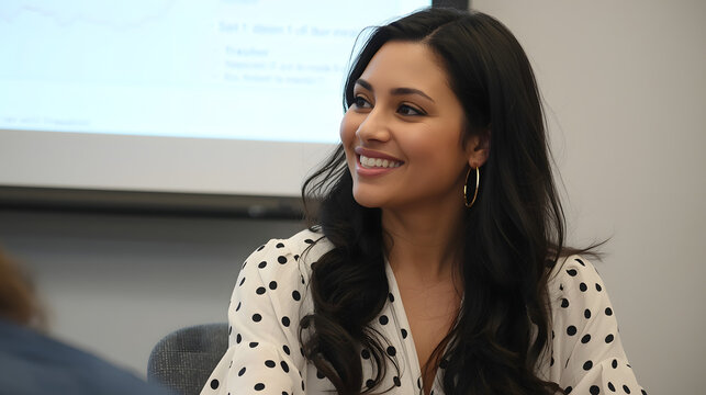 Smiling young businesswoman in professional meeting room wearing polka dot blouse, confident and engaged in conversation, representing success, communication, and positive corporate collaboration