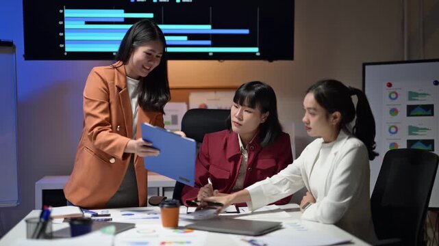 Three women are sitting at a table with a blue folder in front of them. They are smiling and seem to be discussing something important