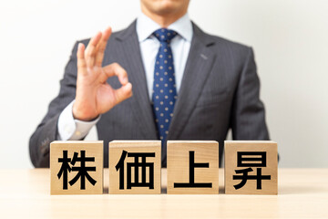 「株価上昇」と書かれたブロックとOKポーズをするビジネスマン