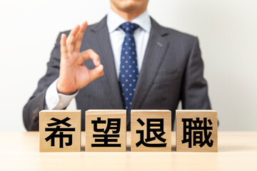 「希望退職」と書かれたブロックとOKポーズをするビジネスマン
