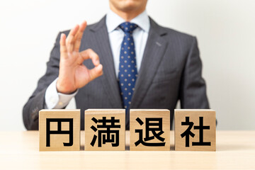 Obraz premium 「円満退社」と書かれたブロックとOKポーズをするビジネスマン