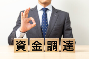 「資金調達」と書かれたブロックとOKポーズをするビジネスマン