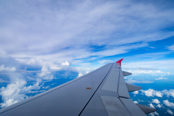 a wing of flying transportation jet plane with a red winglet in deep blue transparent sky background and a cloudy atmosphere below