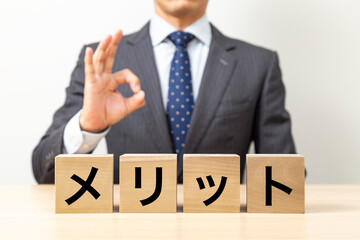 「メリット」と書かれたブロックとOKポーズをするビジネスマン