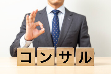 「コンサル」と書かれたブロックとOKポーズをするビジネスマン