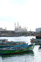 Naklejka premium Traditional fishing boats crowded in the harbor, dwarfed by massive modern container cranes and a cargo ship, symbolizing the contrasting economies and technologies of a coastal city