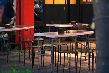 Taiwan - Oct. 26, 2025: Empty outdoor seating area with round metal stools arranged around rectangular tables, red building wall in background, evening ambient light.