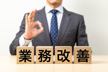 「業務改善」と書かれたブロックとOKポーズをするビジネスマン