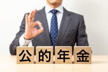 Obraz premium 「公的年金」と書かれたブロックとOKポーズをするビジネスマン