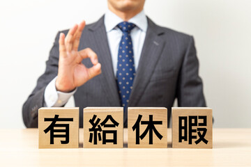 「有給休暇」と書かれたブロックとOKポーズをするビジネスマン