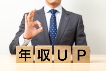 「年収UP」と書かれたブロックとOKポーズをするビジネスマン