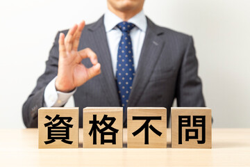 「資格不問」と書かれたブロックとOKポーズをするビジネスマン