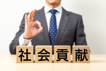 「社会貢献」と書かれたブロックとOKポーズをするビジネスマン