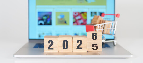 2025 end year to Happy New Year 2026 block with shopping trolley cart on table. E commerce, online shopping, finance, consumer economy and celebration concepts