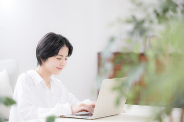 Fototapeta premium 観葉植物の緑がある部屋でパソコンをする女性の主婦やデザイナーのリモートワークや在宅などのイメージ