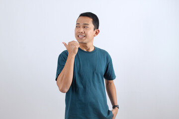 Smiling Asian man pointing aside with thumb on white background