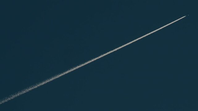 Airplane flying high above leaving long contrails in a clear blue sky