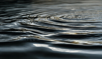 Close up abstract view of dark water surface with ripples and reflections creating organic patterns