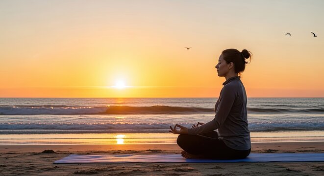 A woman meditating on a beach at sunset.