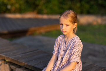 Young girl sitting on a wooden bench outdoors during sunset