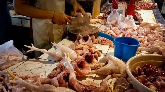 A butcher at a traditional market cuts fresh chicken meat for a customer. The scene captures the hustle and vibrant atmosphere of daily market life