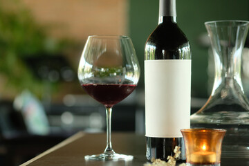 Elegant still life featuring a wine glass and a bottle of red wine, beside a lit candle and a carafe. The scene is set with a soft focus and inviting atmosphere.