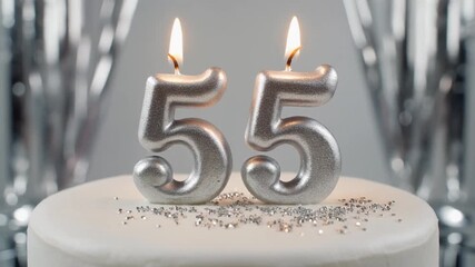 A minimalist white birthday cake featuring glowing silver candles for a fifty-fifth anniversary or birthday party celebration