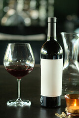 A close-up shot of a wine bottle and a glass of red wine, with a candle and a decanter in the blurred background. A concept of relaxation, celebration, or a fine dining experience