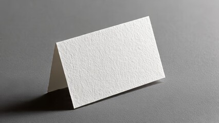 Blank white folded card standing on a textured gray surface blank card