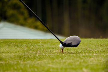 グリーンのピンに置かれたゴルフボールを狙うクラブ