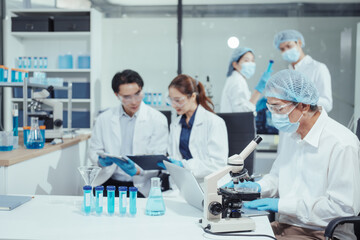 Team of Asian scientists working in modern laboratory equipped microscopes, chemical reagents,...