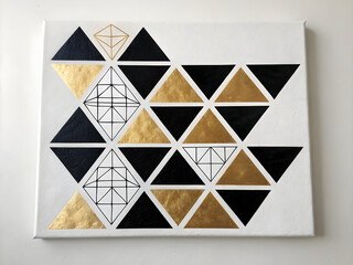 Abstract geometric artwork with black and metallic gold triangles and linear diamond shapes painted on white canvas.
