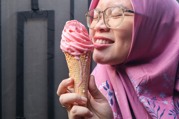 Beautiful Asian muslim woman smiling, holding and enjoying delicious strawberry ice cream waffle...