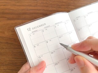 A woman's hands filling out a December schedule book on a wooden table
