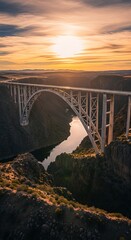 Dramatic Golden Hour Sunset Illuminates Grand Arch Bridge Spanning Deep Canyon Gorge with Reflective River.
