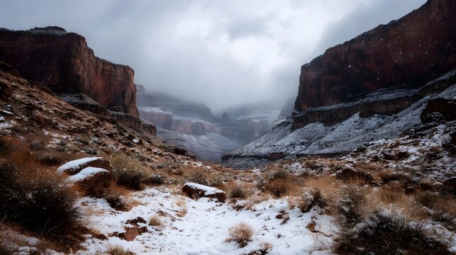 Winter snow falls on a canyon landscape with rugged cliffs and dry vegetation under a cloudy sky - Powered by Adobe